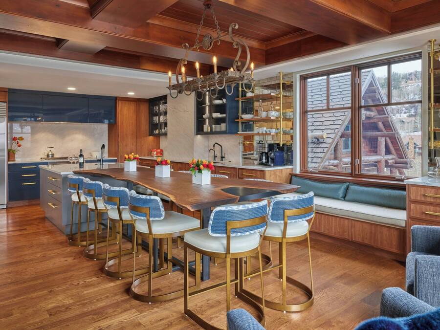 A modern kitchen with a central island, bar stools, and a view of a cabin through large windows.