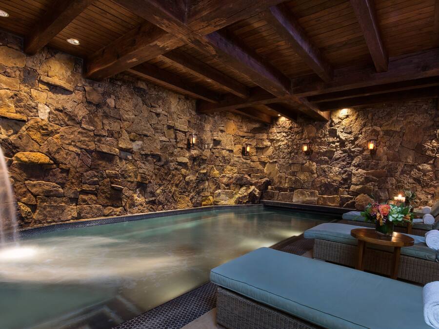 A stone-walled indoor pool with a waterfall feature, lounge seating, and ambient lighting.