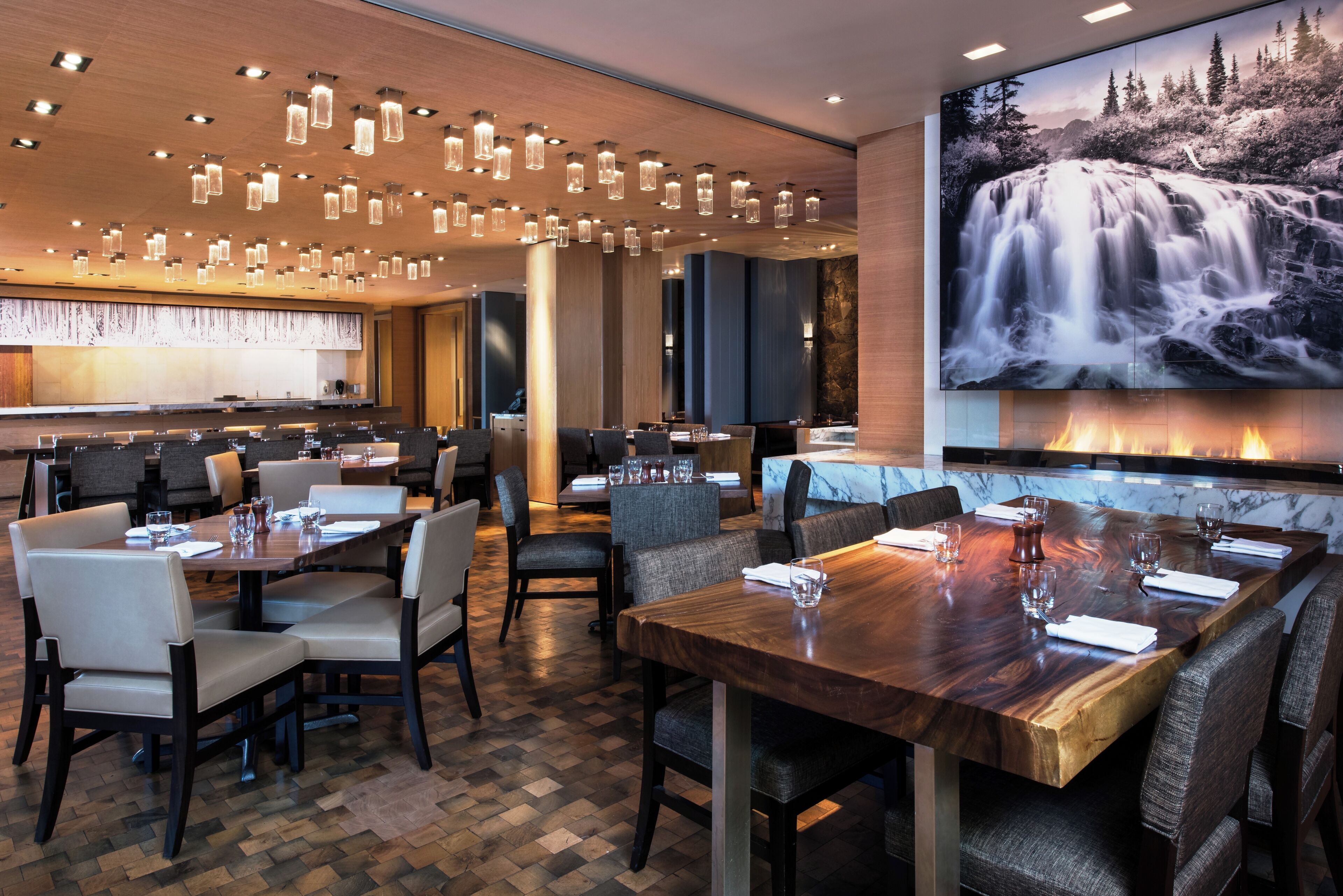 A restaurant with multiple dining tables, chairs, and a large waterfall painting on the wall.
