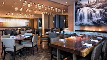 A restaurant with multiple dining tables, chairs, and a large waterfall painting on the wall.