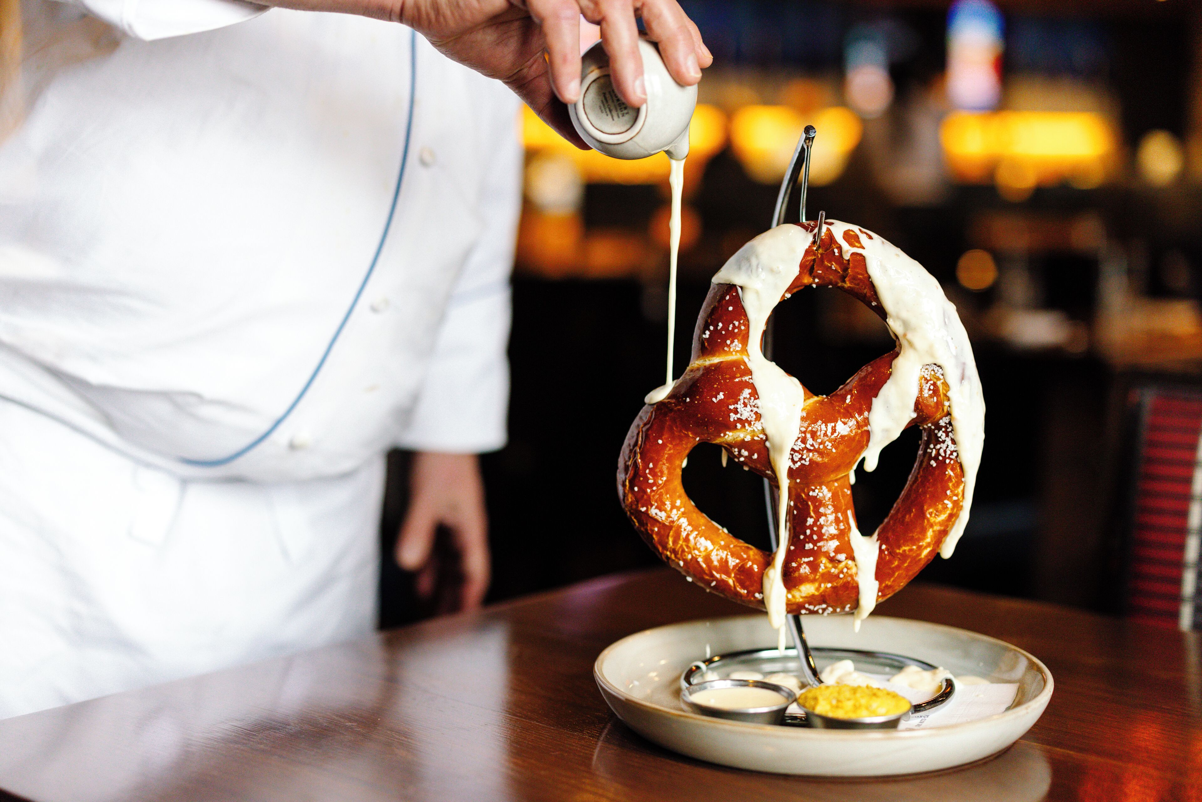 A person pouring sauce over a pretzel on a plate.