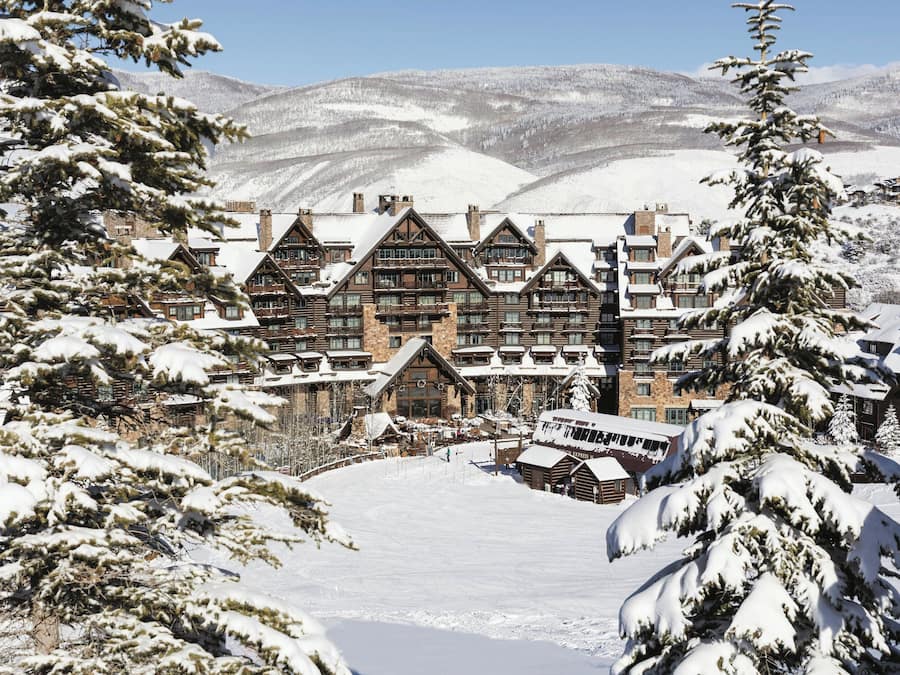 A large lodge with multiple buildings, surrounded by snow-covered trees and mountains.