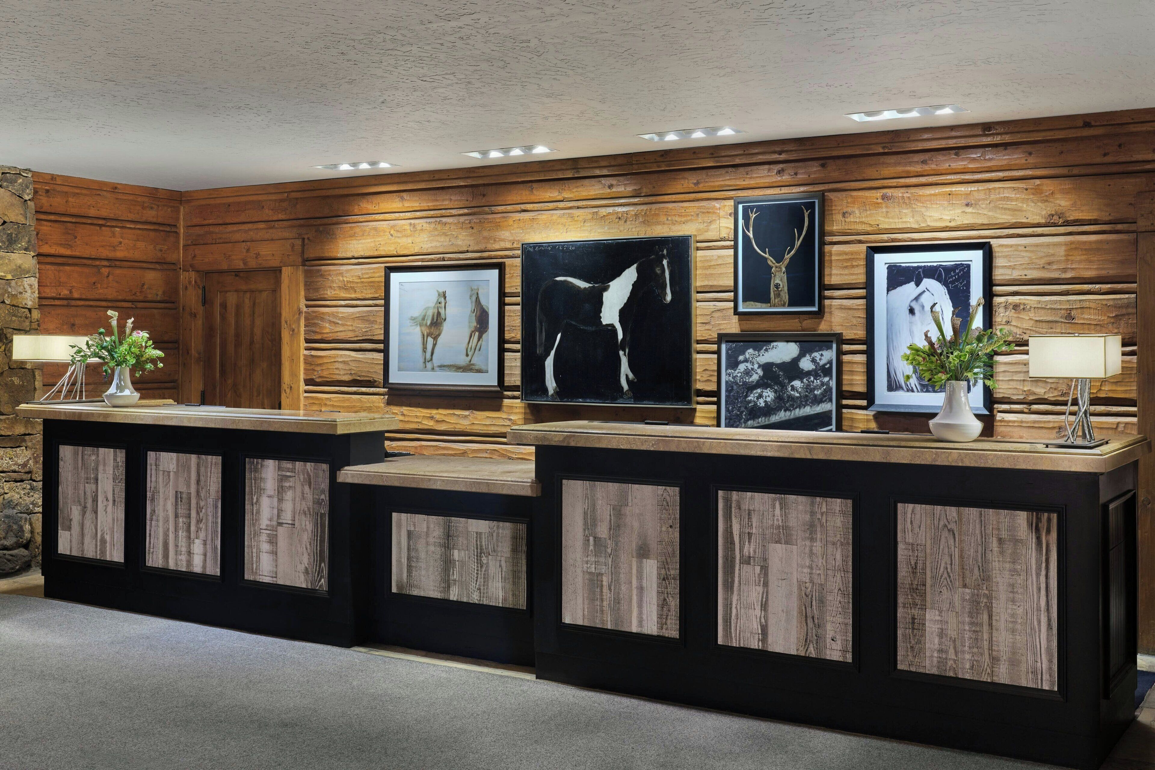 A reception desk with wooden paneling, framed artwork, and two lamps.