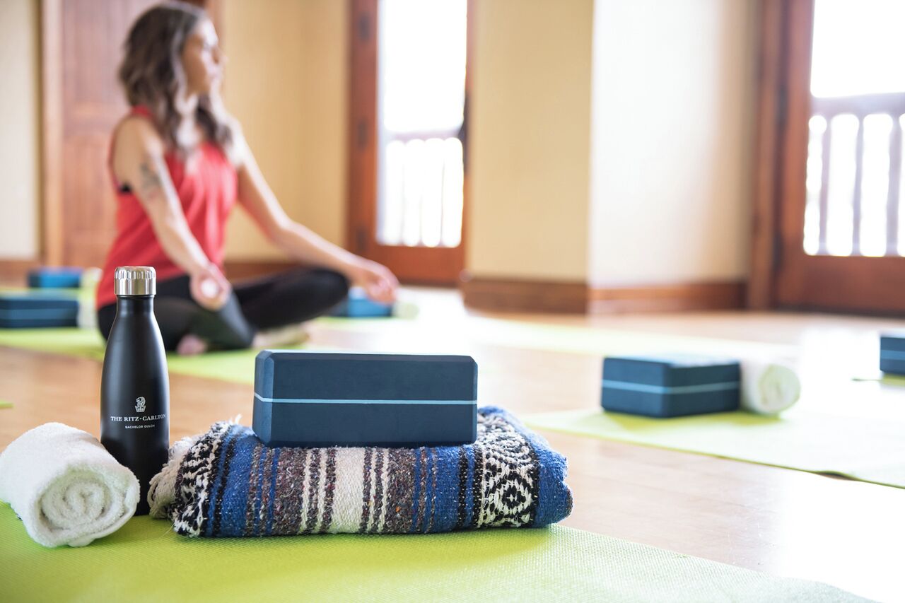 Eine Yogamatte, ein zusammengerolltes Handtuch, eine Wasserflasche und ein Yoga-Block liegen auf dem Boden.