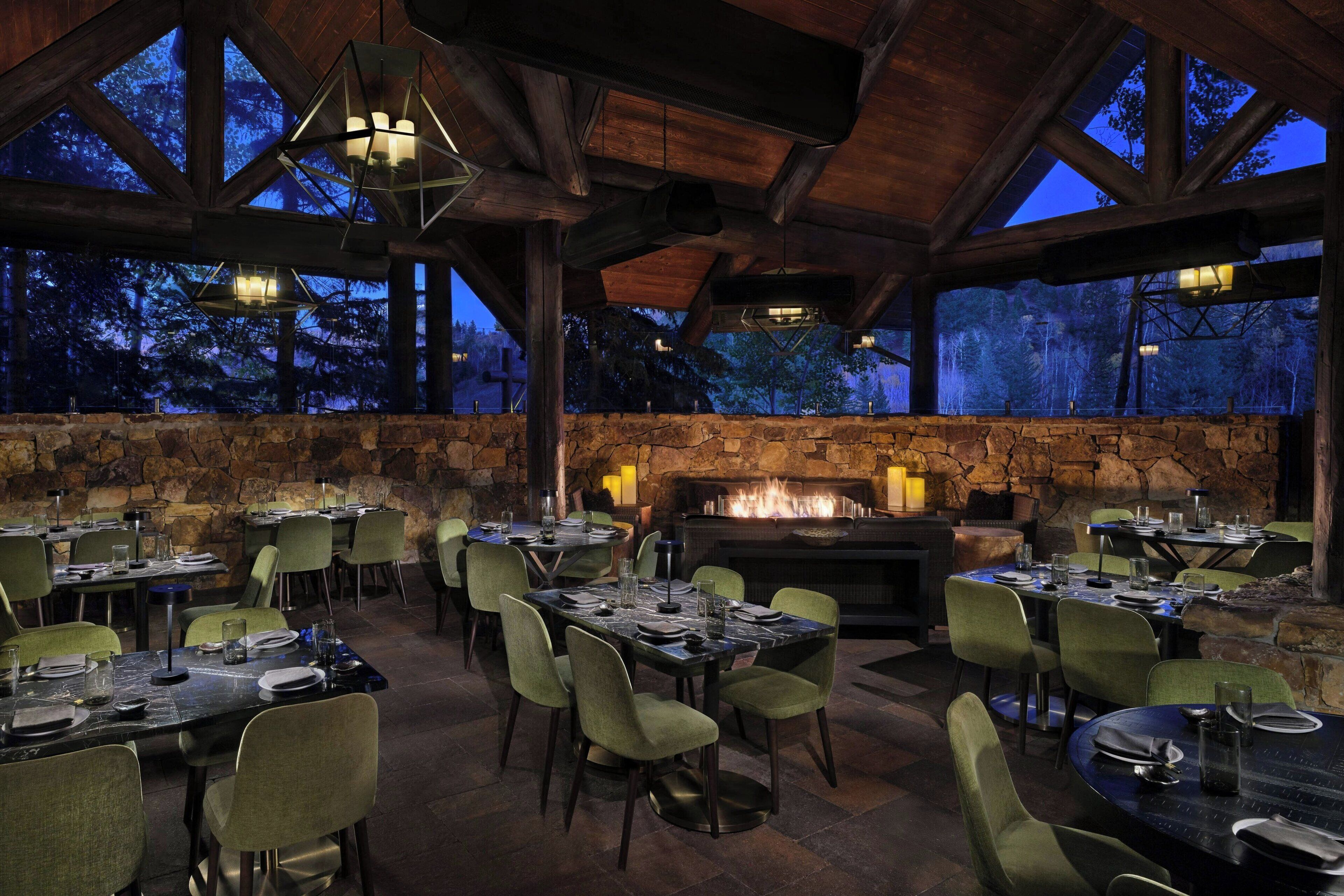 An outdoor dining area with stone walls, wooden beams, and tables set for dining.