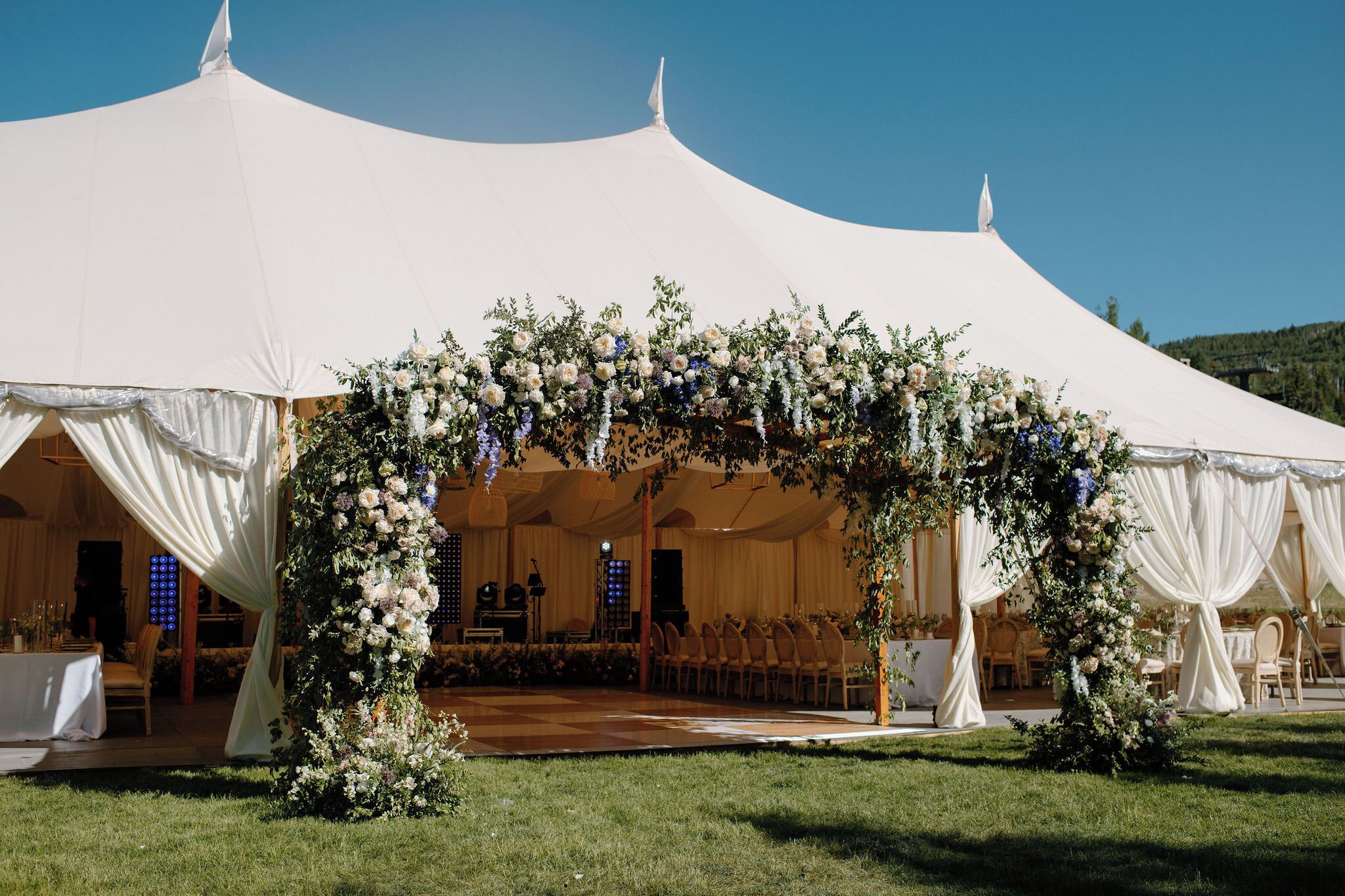 A tented wedding venue with a stage, chairs, and floral decorations.
