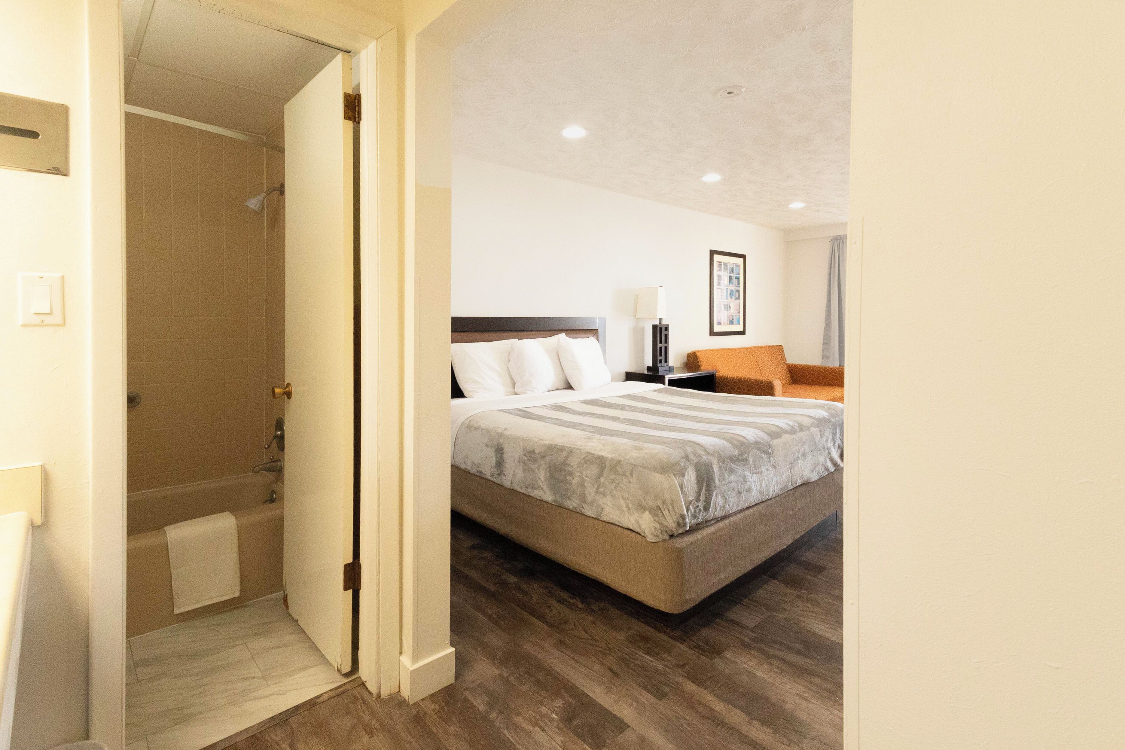 Ein Hotelzimmer mit Bett, Nachttisch, Lampe, Stuhl und Duschbereich.