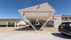A parking lot with a building featuring a unique slanted roof design. - Circle S Motel Cozad I-80 (Cozad)