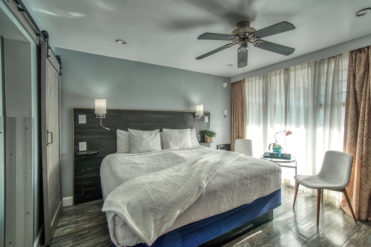 A bedroom with a bed, a ceiling fan, a bedside table with a lamp, and a chair.