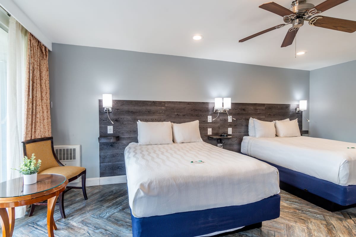 A hotel room with two beds, a ceiling fan, and a table with a chair.