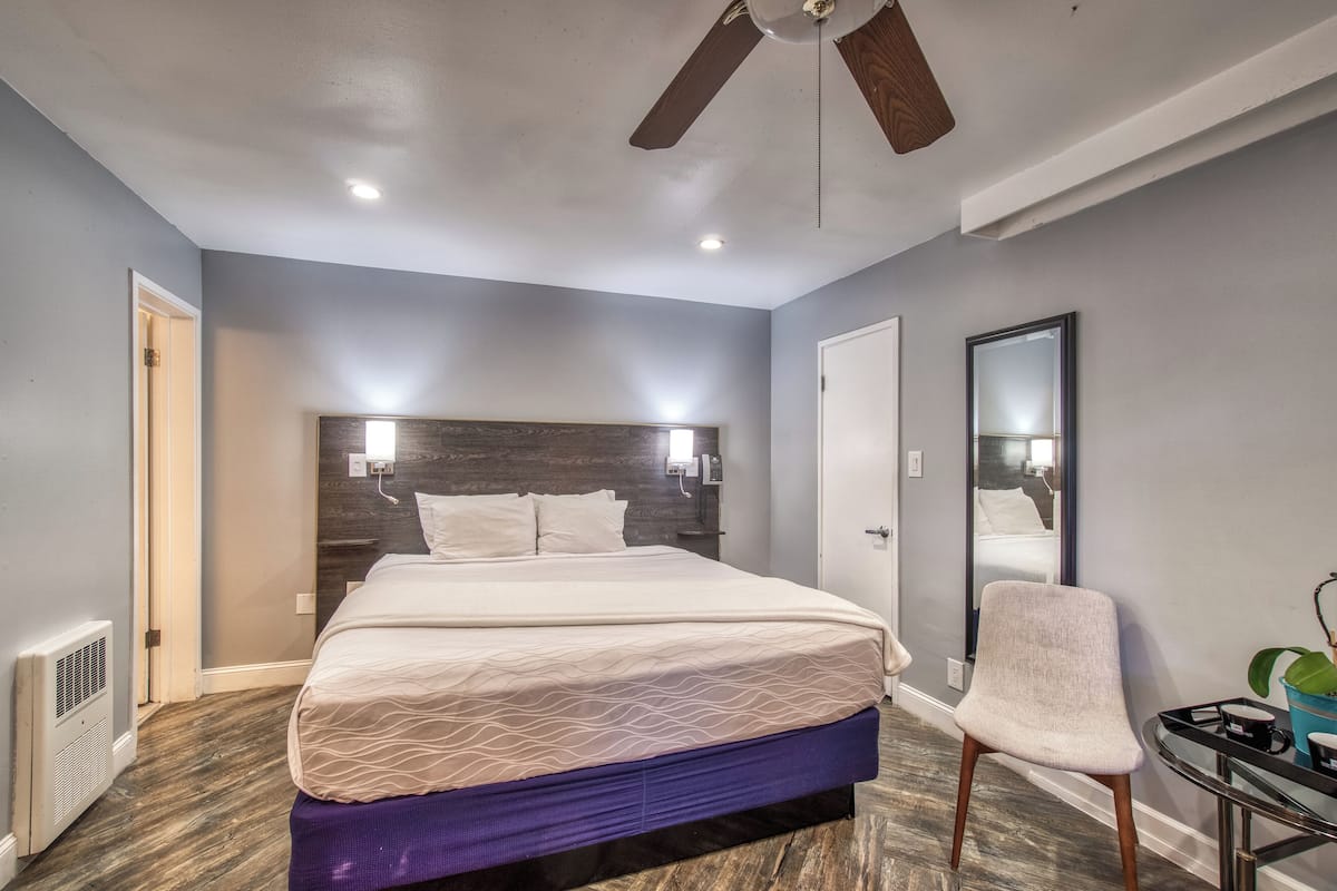 A bedroom with a bed, a ceiling fan, a mirror, and a chair.