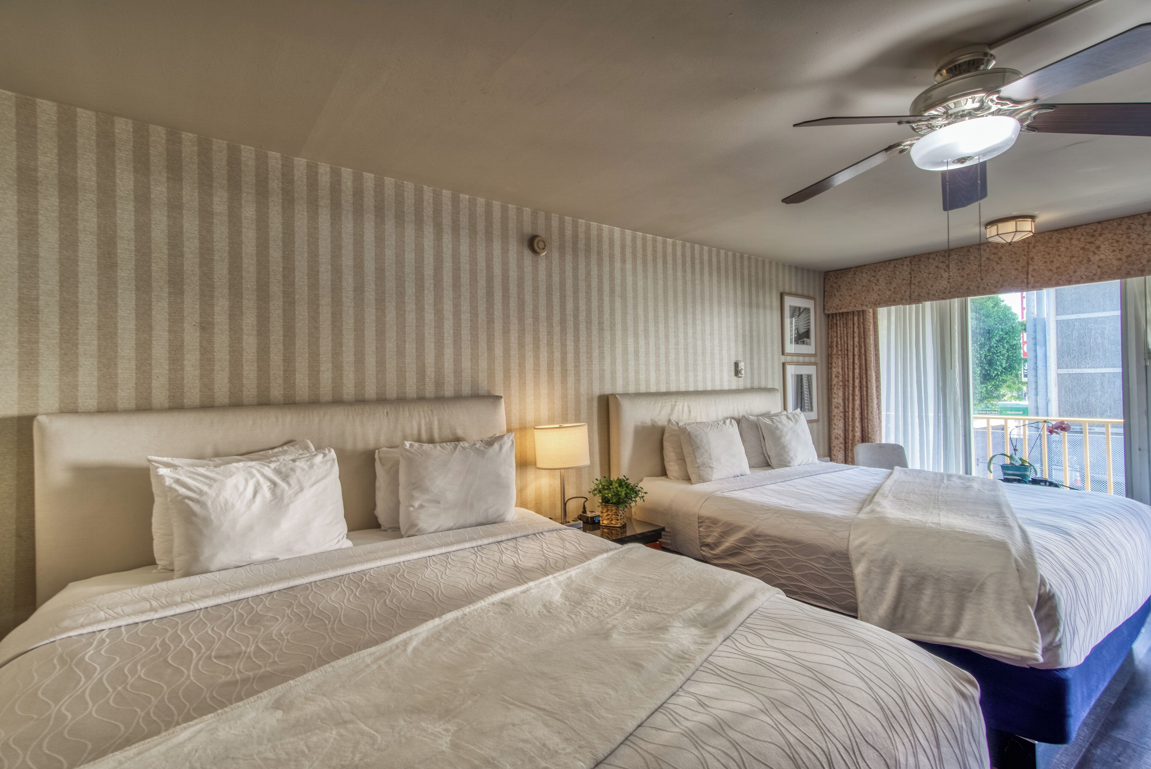 Ein Hotelzimmer mit zwei Betten, einem Deckenventilator und einem Fenster mit Vorhängen.