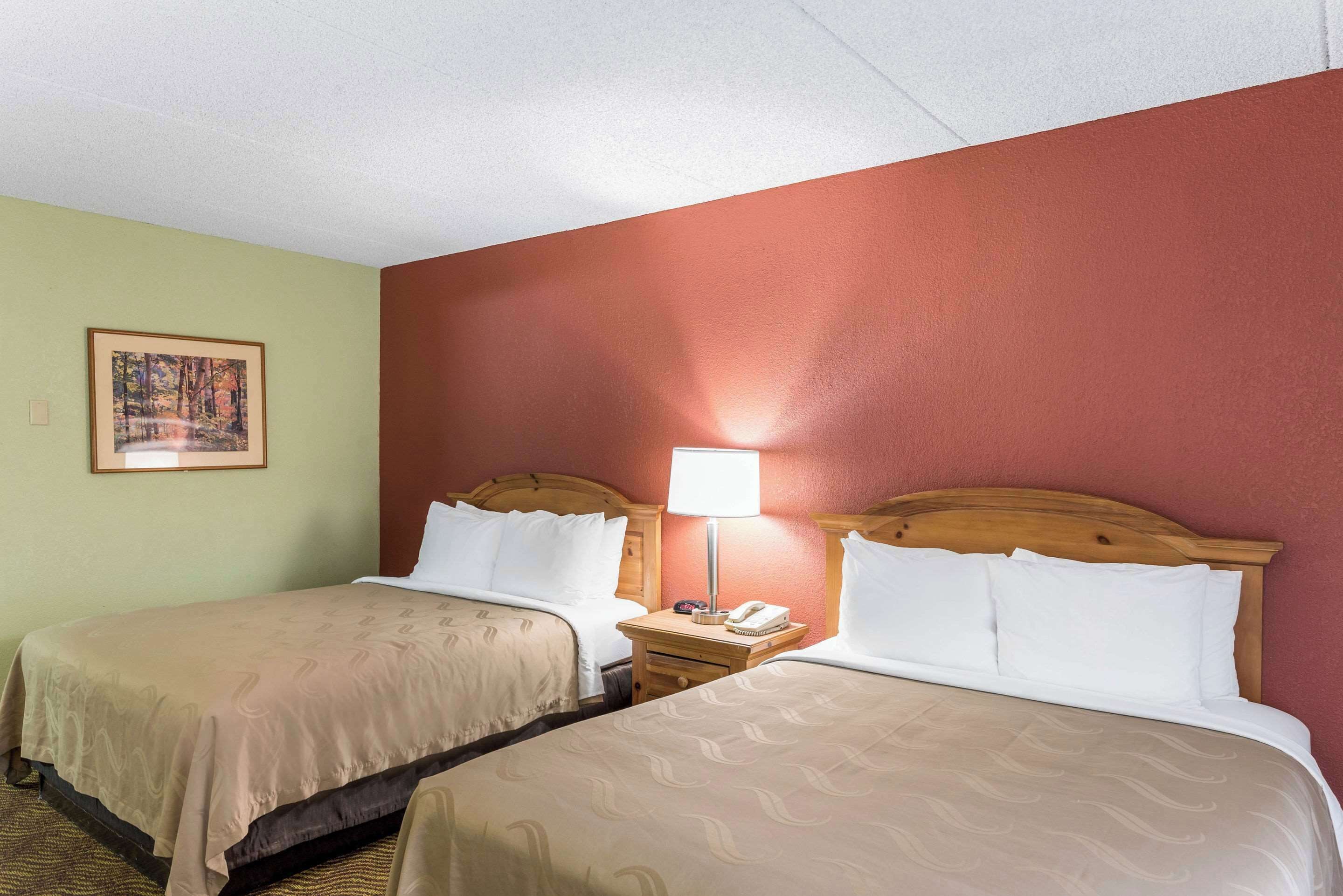 A hotel room with two beds, a nightstand with a lamp, and a framed picture on the wall.