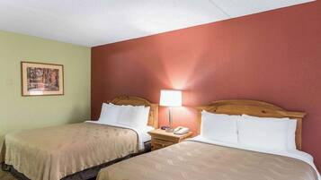 A hotel room with two beds, a nightstand with a lamp, and a framed picture on the wall.