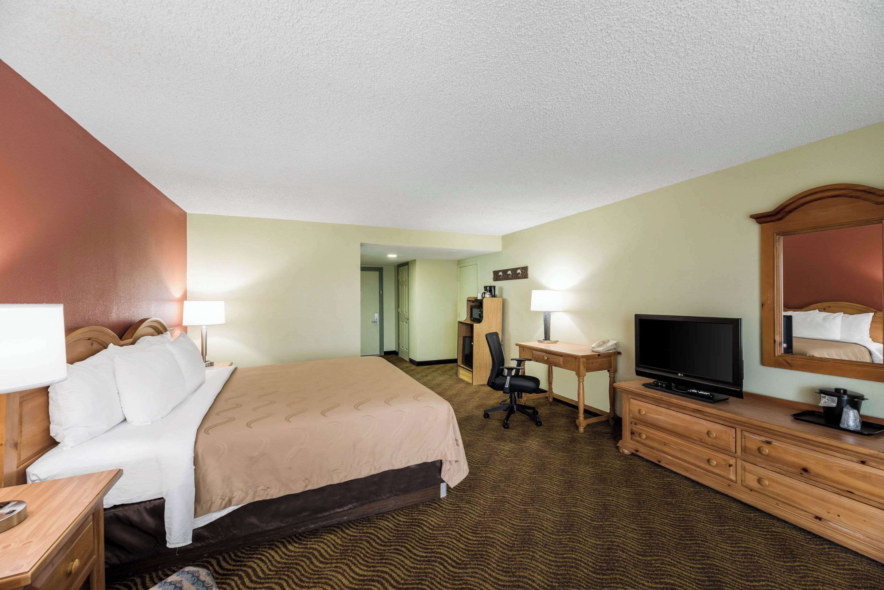 A hotel room with a bed, desk, television, dresser, and a mirror.