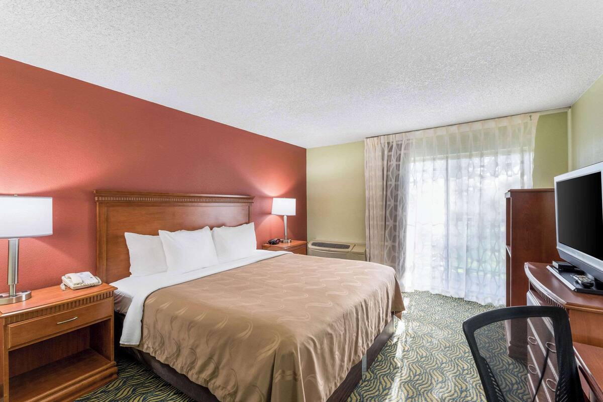 A hotel room with a large bed, a desk with a television, a telephone, and a lamp.