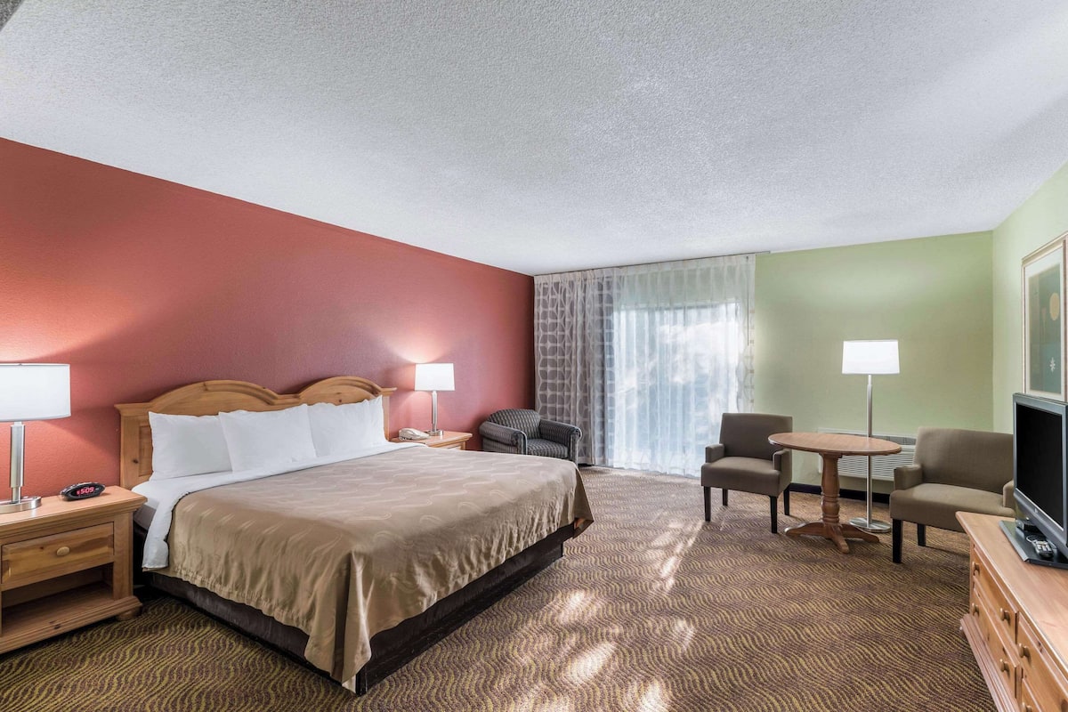 A hotel room with a bed, two bedside tables, a chair, a small round table, and a television.