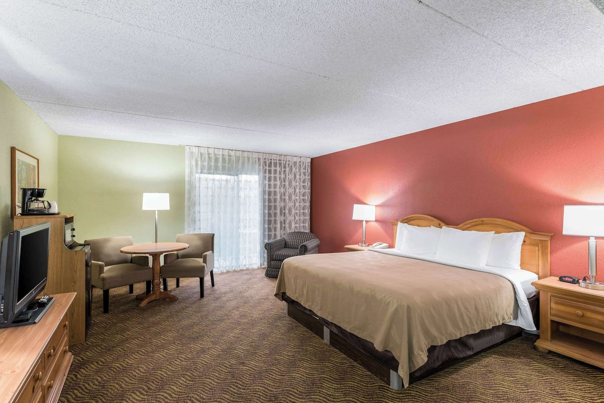 A hotel room with a bed, a desk, a chair, a television, and a window with curtains.