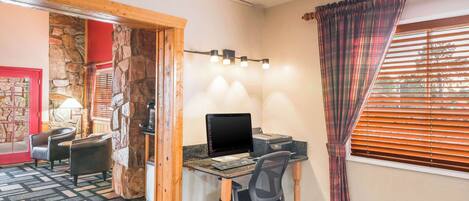 A room with a wooden desk, a computer, and two chairs. There is a stone wall and a window with blinds.