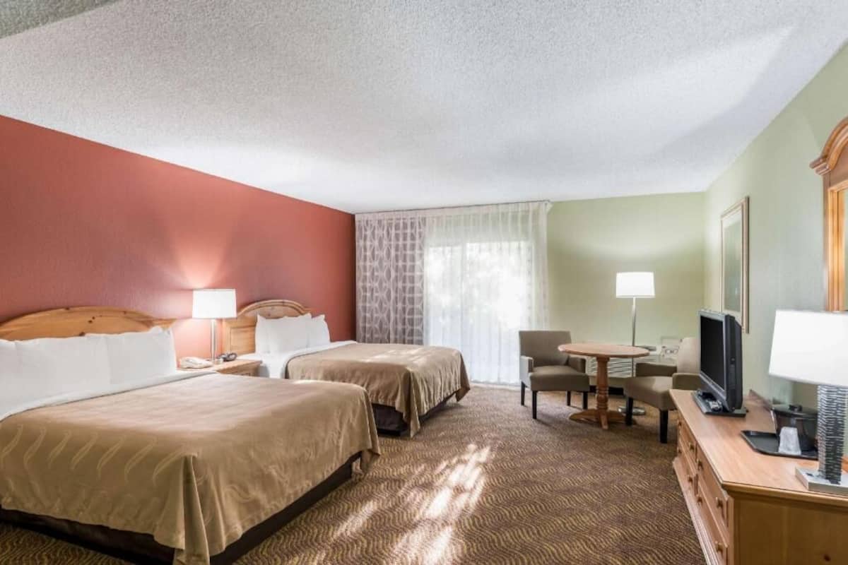 A hotel room with two beds, a desk with a chair, a television, and a window with curtains.
