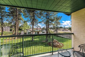 A balcony with a metal railing, overlooking a well-maintained lawn with trees and a distant view of houses.