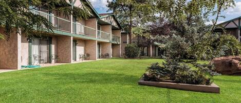 A building with a green balcony, a well-maintained lawn, and a variety of trees and shrubs.