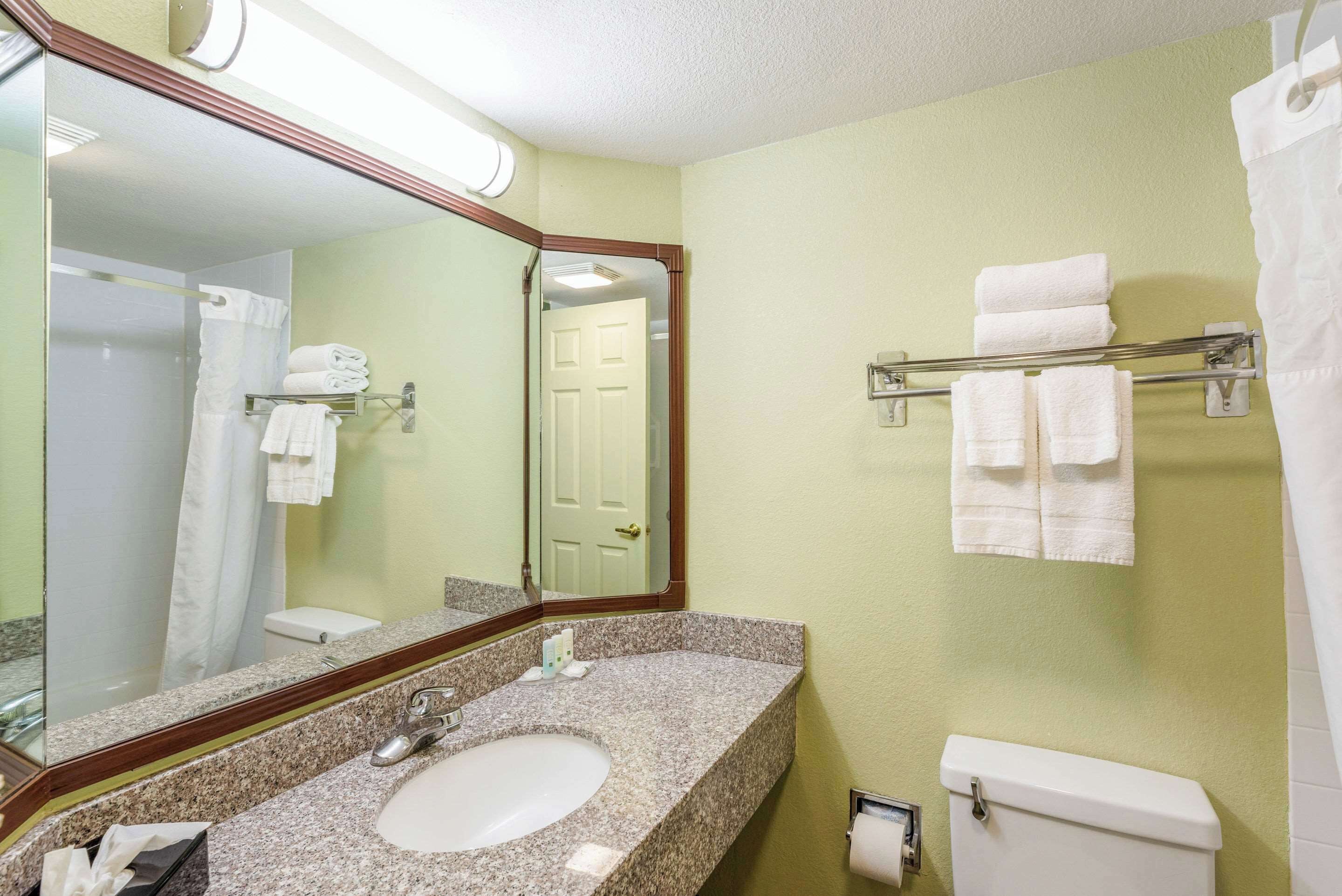 A bathroom with a granite countertop sink, a mirror, a toilet, and a towel rack with folded towels.