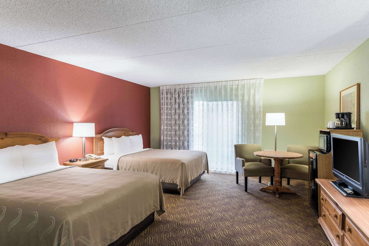 A hotel room with two beds, a desk with a chair, a television, and a coffee maker.