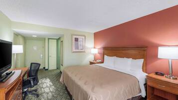 A hotel room with a bed, desk, chair, television, and a nightstand with a lamp.