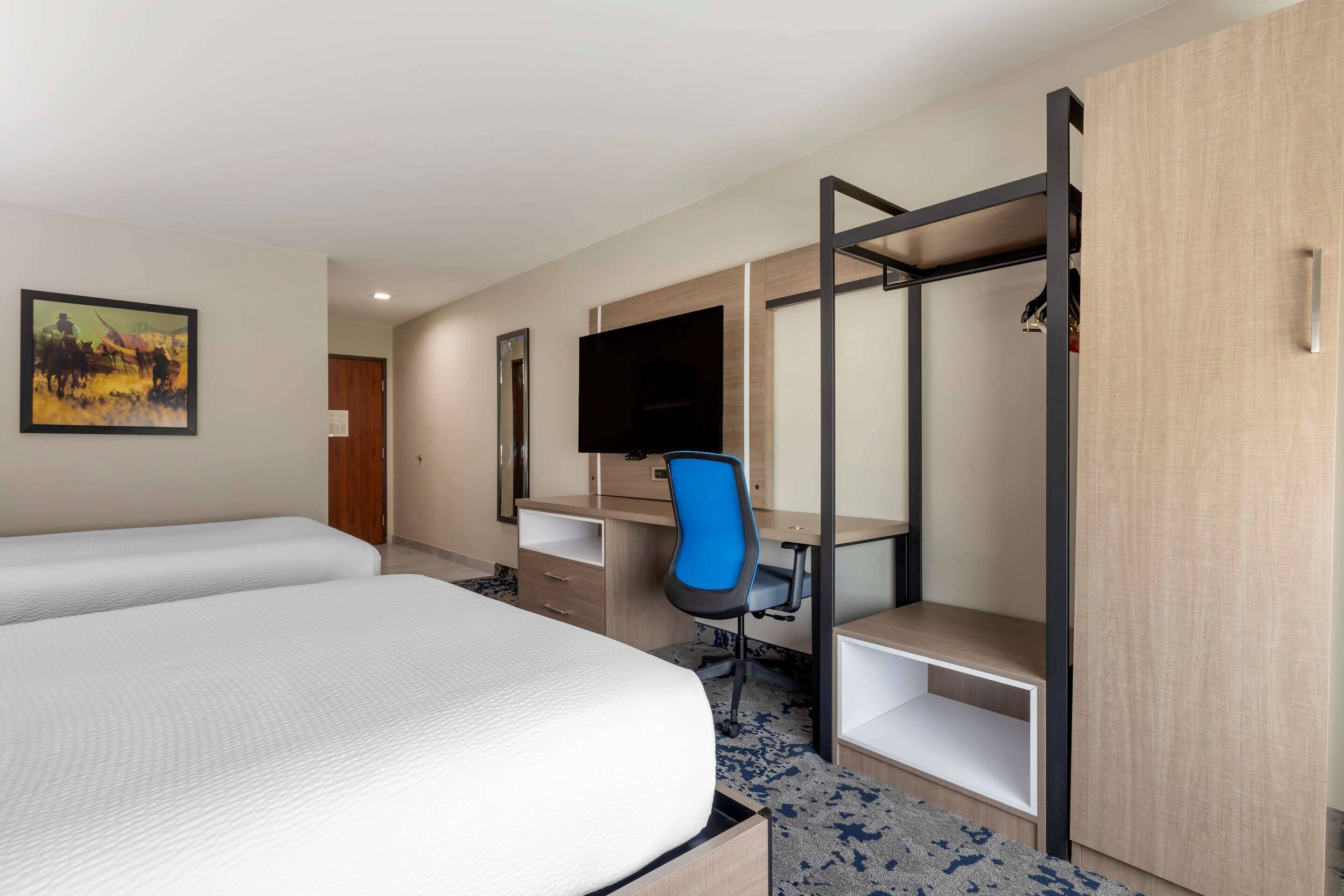 A hotel room with two beds, a desk, a chair, a TV, and a wardrobe.