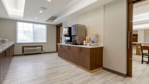 Une cuisine moderne équipée d’une machine à café intégrée, d’un four à micro-ondes et d’un petit réfrigérateur. Une fenêtre laisse entrer la lumière naturelle et offre une vue sur l’extérieur.