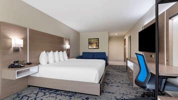 A hotel room with a bed, a desk, a chair, a TV, and a painting on the wall.