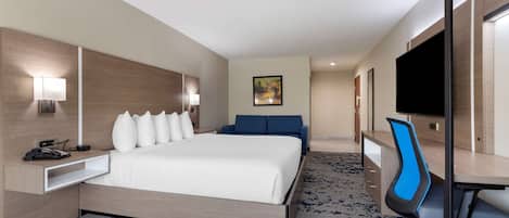 Una habitación de hotel con cama, escritorio, silla, televisor y un cuadro en la pared.