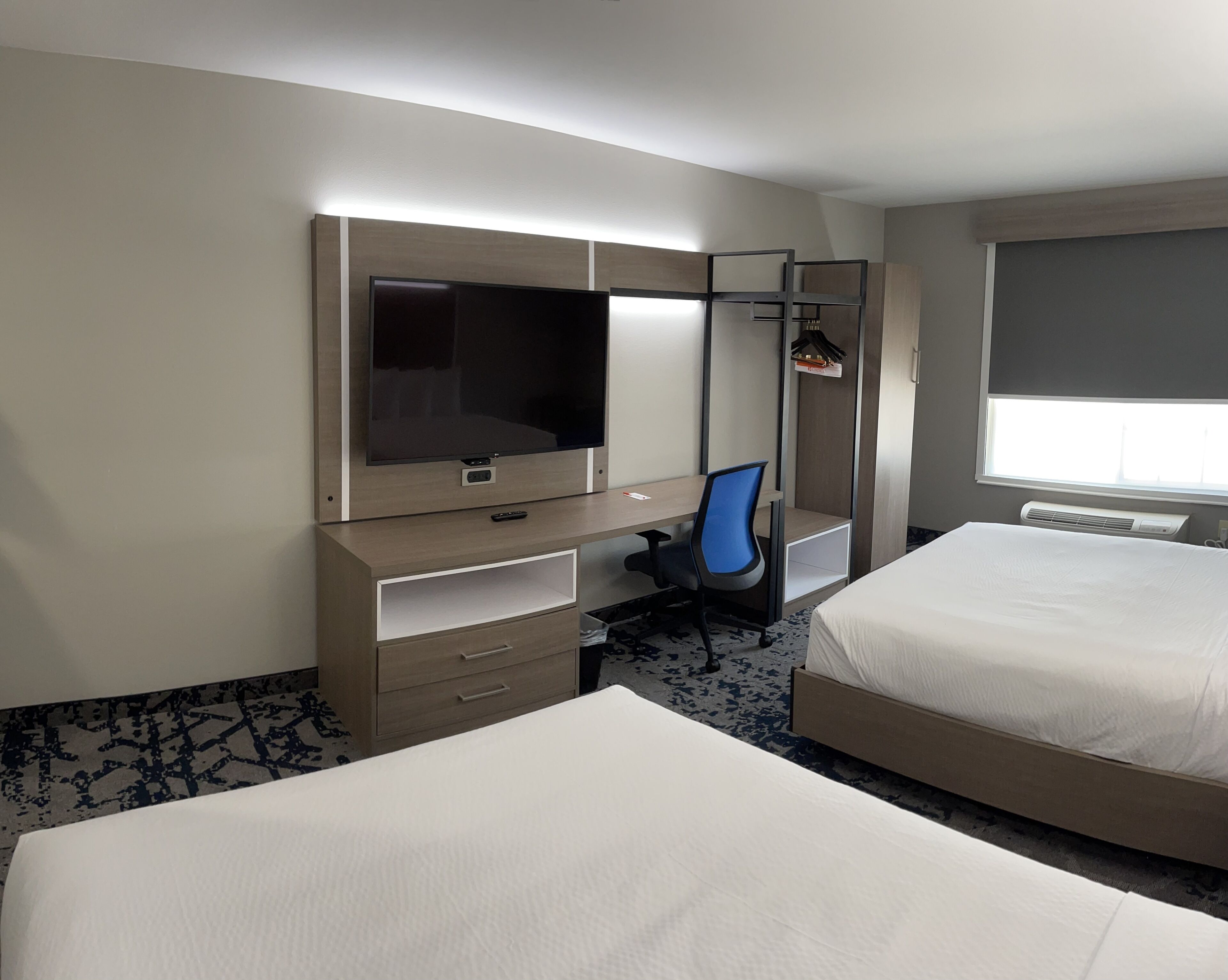 Habitación de hotel con dos camas, un escritorio con silla, televisor y ventana.