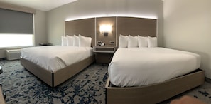 A hotel room with two beds, a bedside table with a lamp, and a large window with a view.