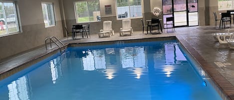 Una piscina interior con agua cristalina, rodeada de sillones y mesas.