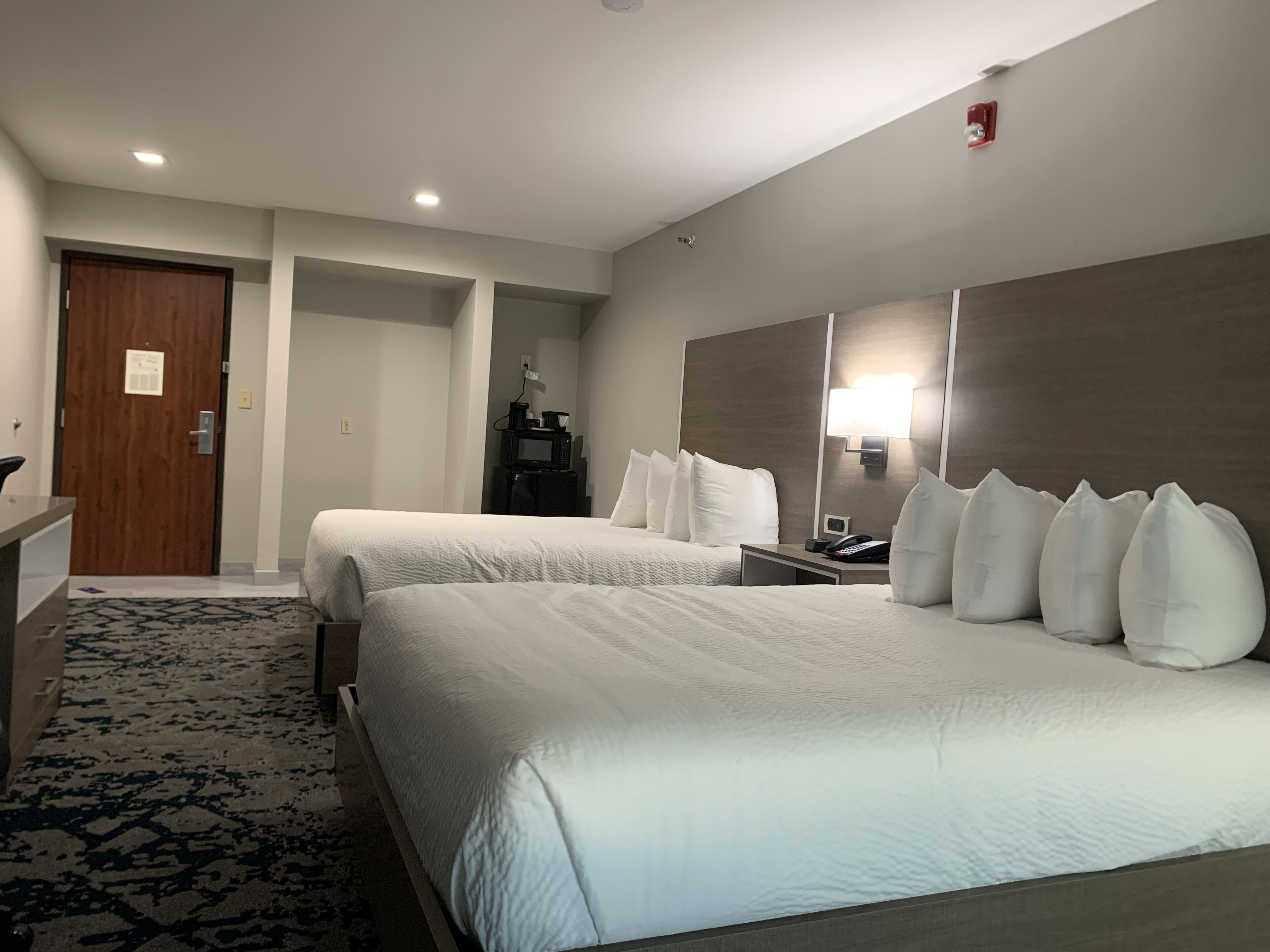 Habitación de hotel con dos camas, un escritorio, una silla, una lámpara de escritorio y un teléfono fijo en la pared.