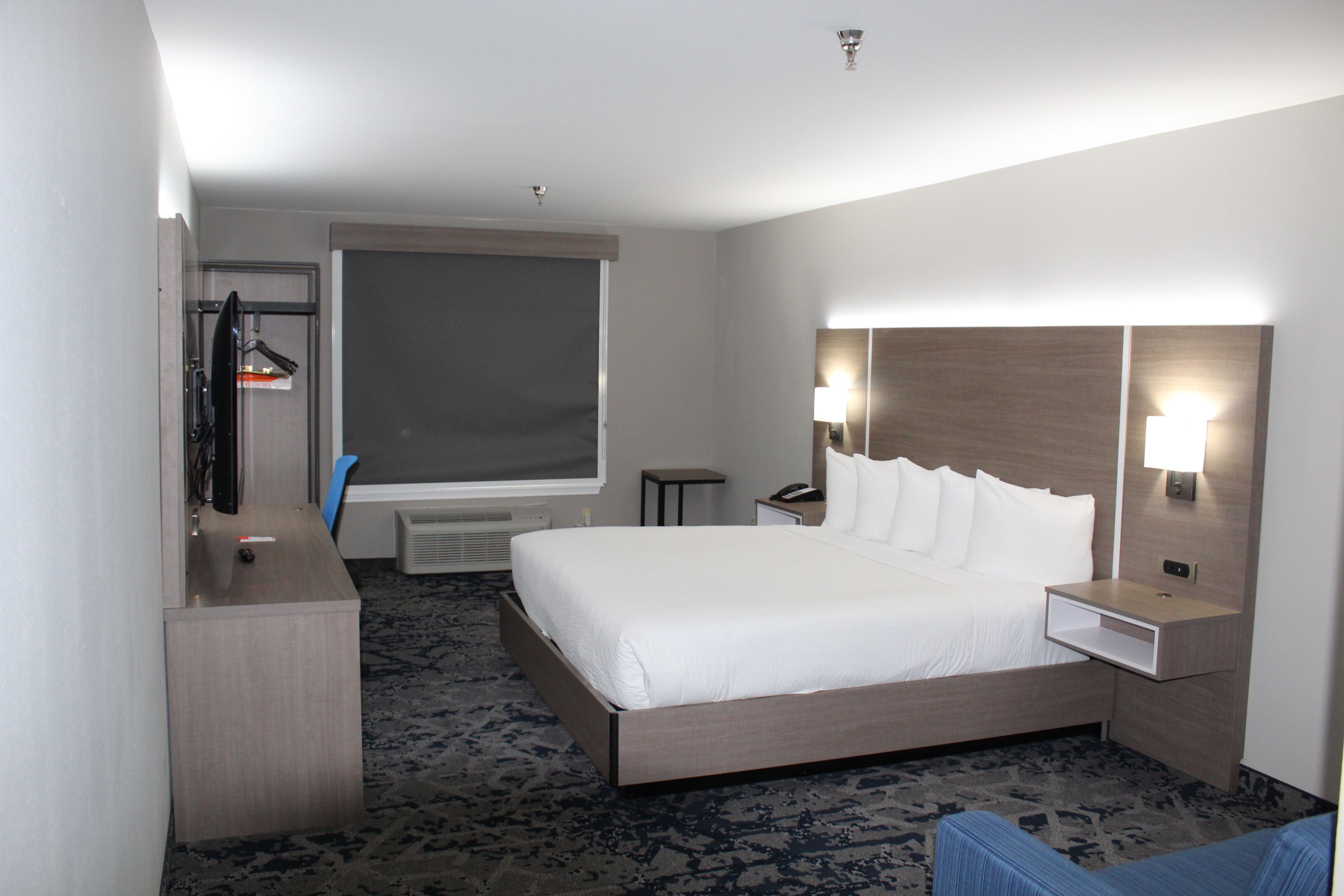 Una habitación de hotel con una cama grande, un escritorio, una silla, un televisor, una ventana y una mesita de noche con lámpara.