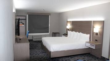 Una habitación de hotel con una cama grande, un escritorio, una silla, un televisor, una ventana y una mesita de noche con lámpara.