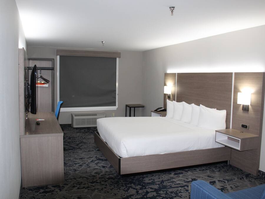 Una habitación de hotel con una cama grande, un escritorio, una silla, un televisor, una ventana y una mesita de noche con lámpara.
