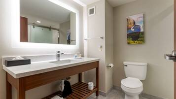 A bathroom with a white sink, wooden vanity, a large mirror, a toilet, and a painting on the wall.