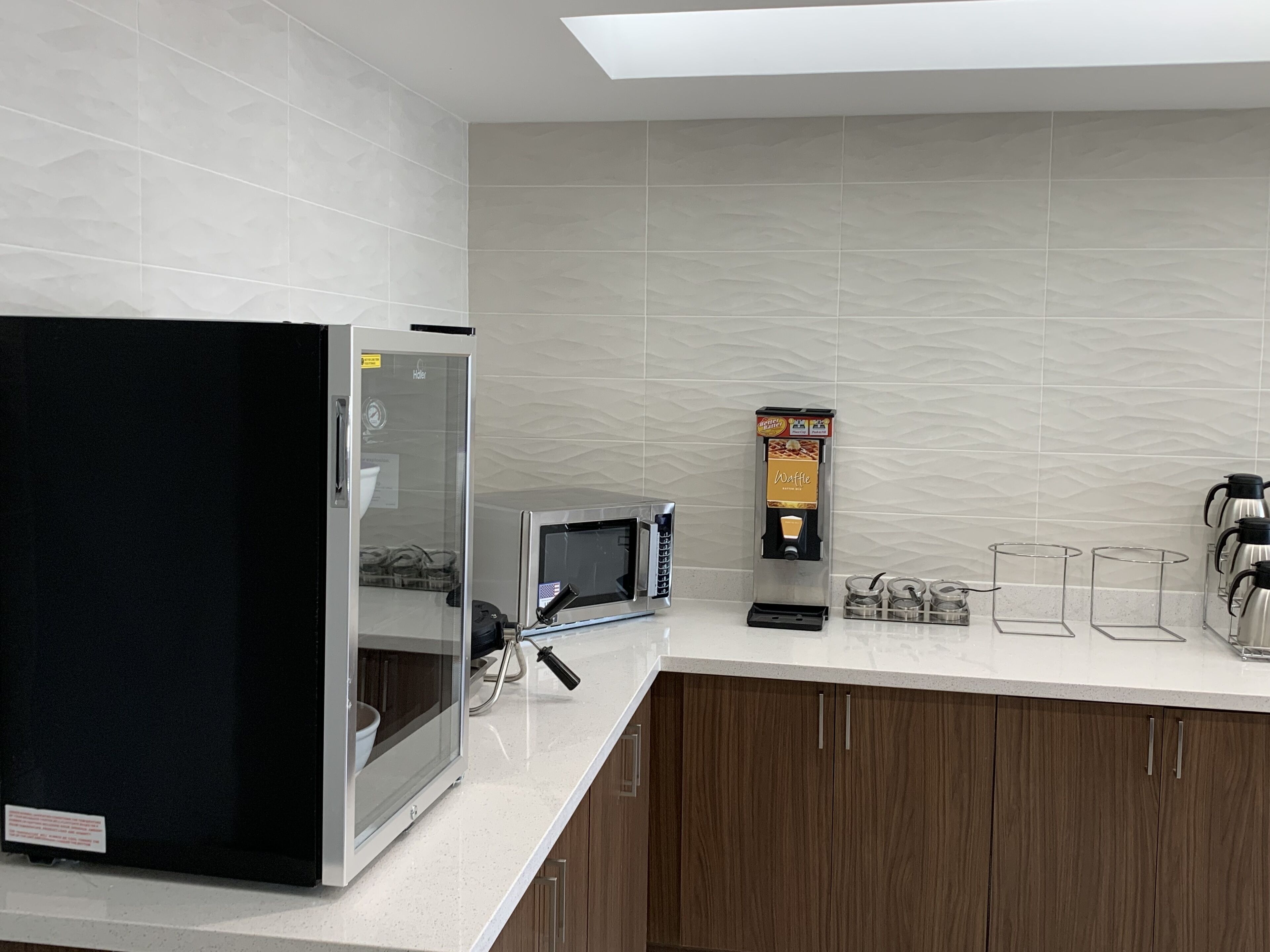 A modern kitchen with a refrigerator, microwave, waffle maker, and coffee maker.