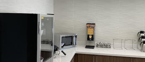 A modern kitchen with a refrigerator, microwave, waffle maker, and coffee maker.