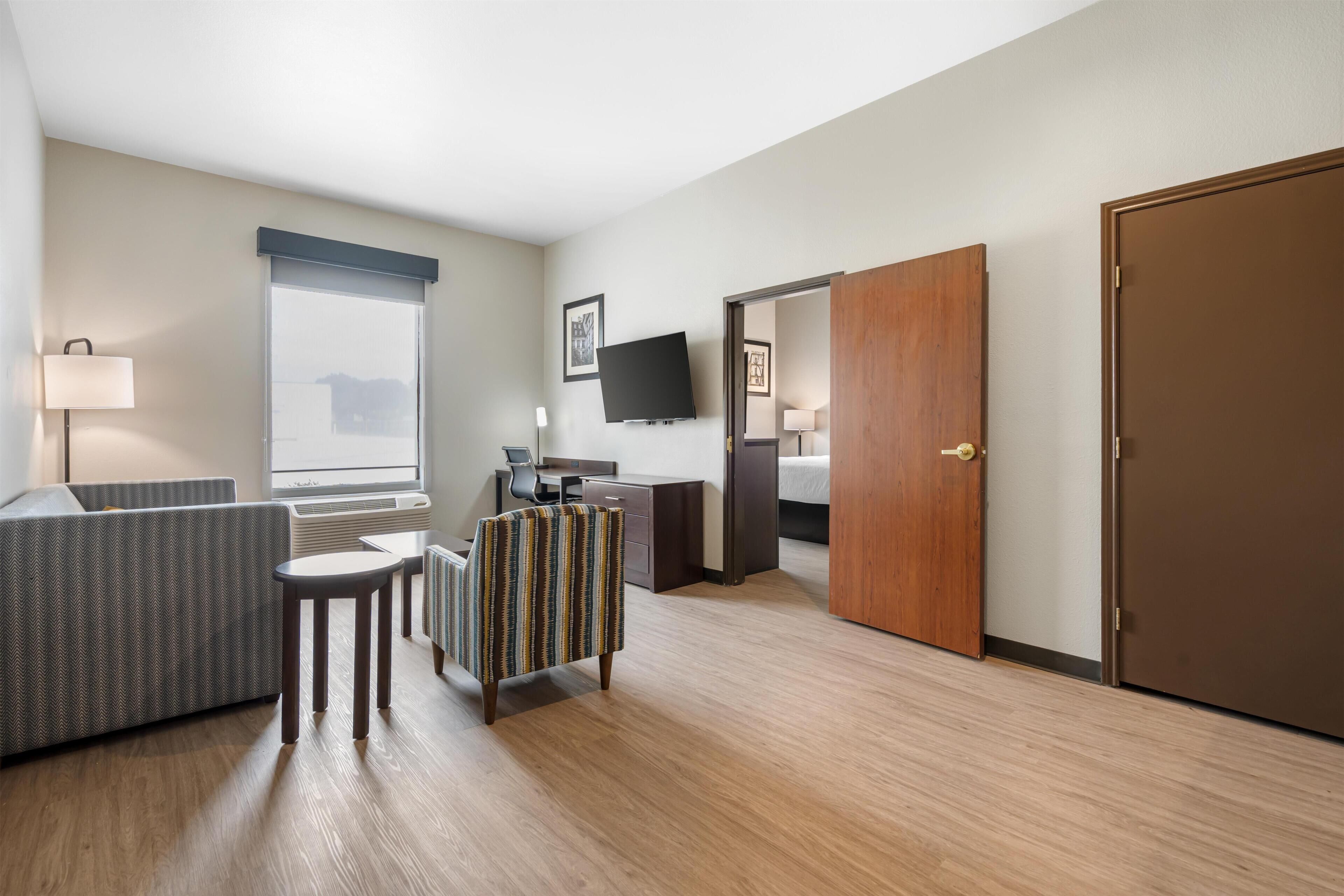 A hotel room with a sofa, a small table, a chair, a TV, a desk, and a wardrobe.