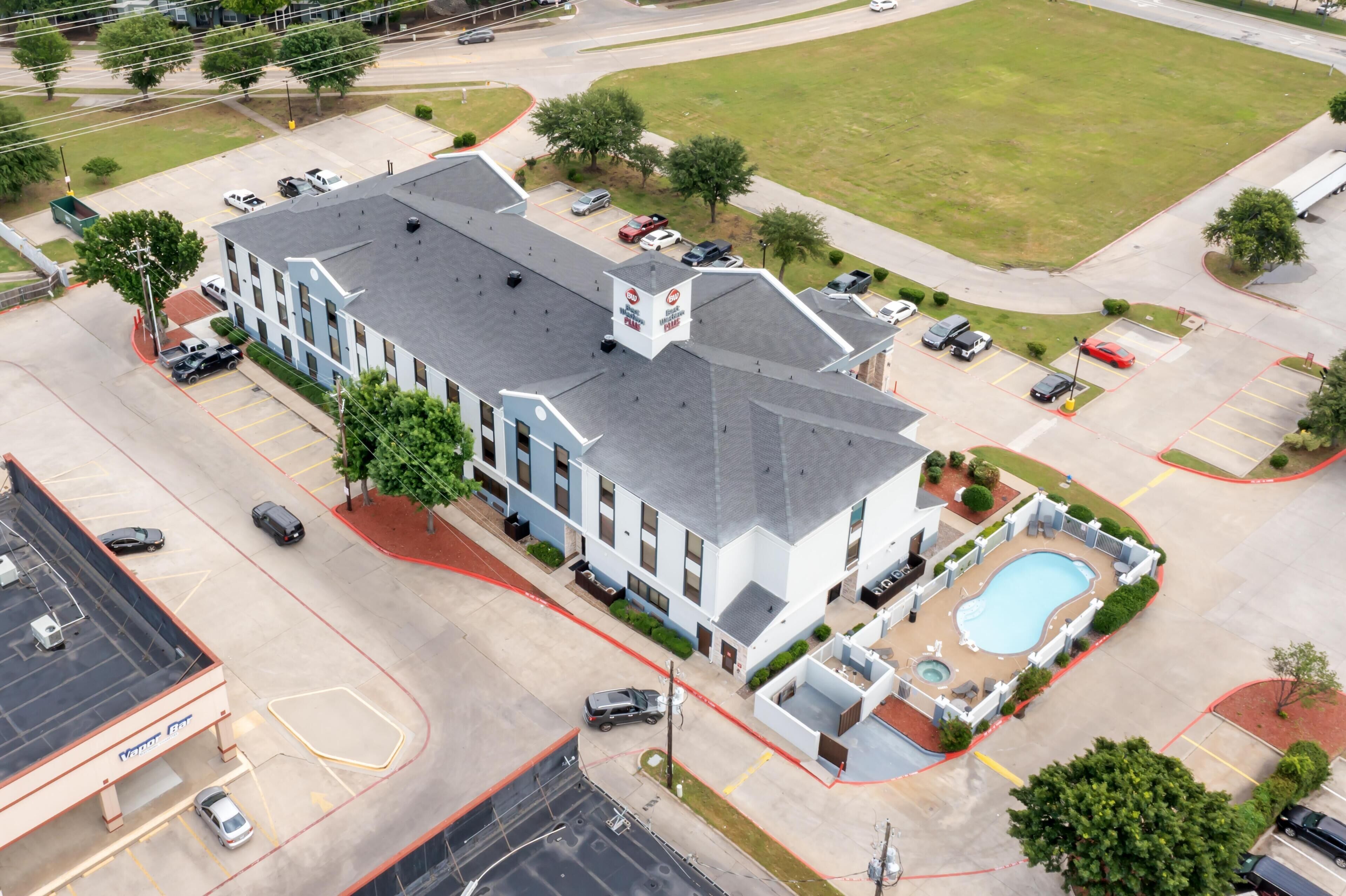 A multi-story hotel with a swimming pool, parking lot, and a large lawn area.