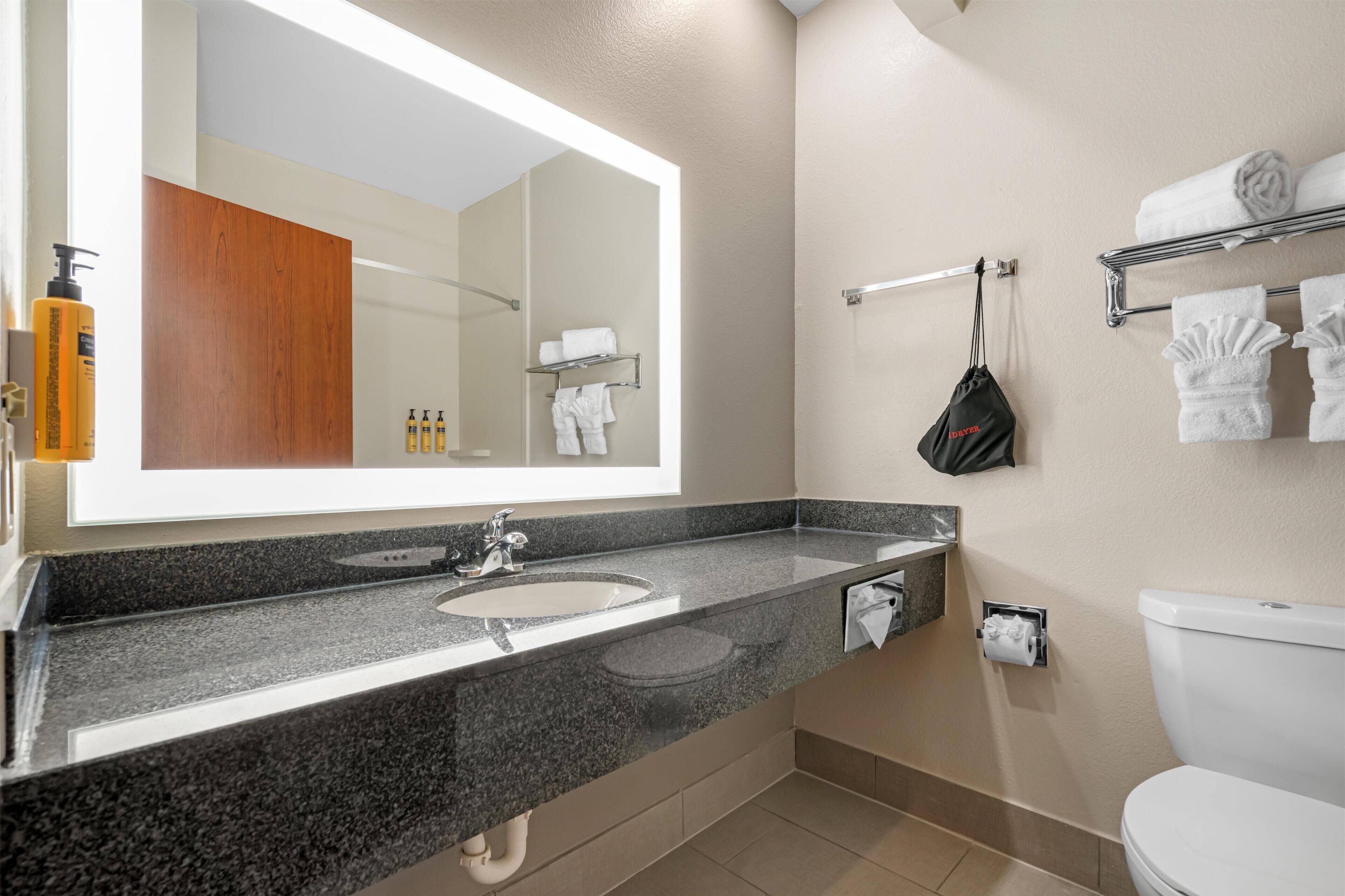 Un baño moderno con encimera de granito, un espejo grande, un lavabo blanco, un inodoro y un toallero con toallas dobladas cuidadosamente.