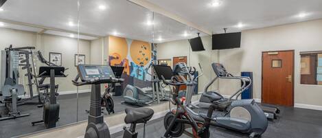 Un gimnasio con equipo de ejercicio, un espejo y una pared con un mural colorido.