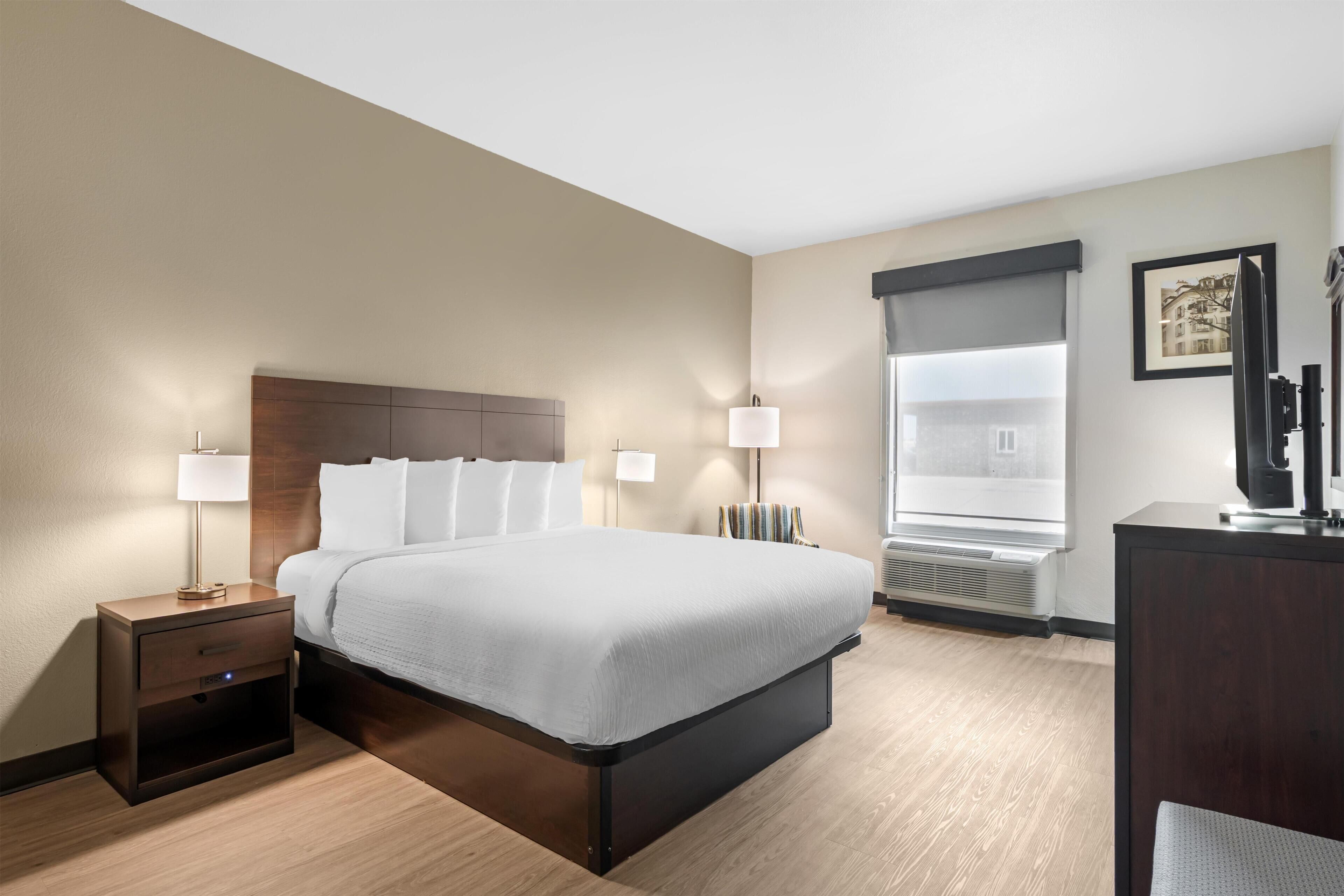 A hotel room with a bed, bedside tables, lamps, a desk, and a large window.