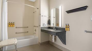 A bathroom with a bathtub, a sink, a mirror, and handrails.