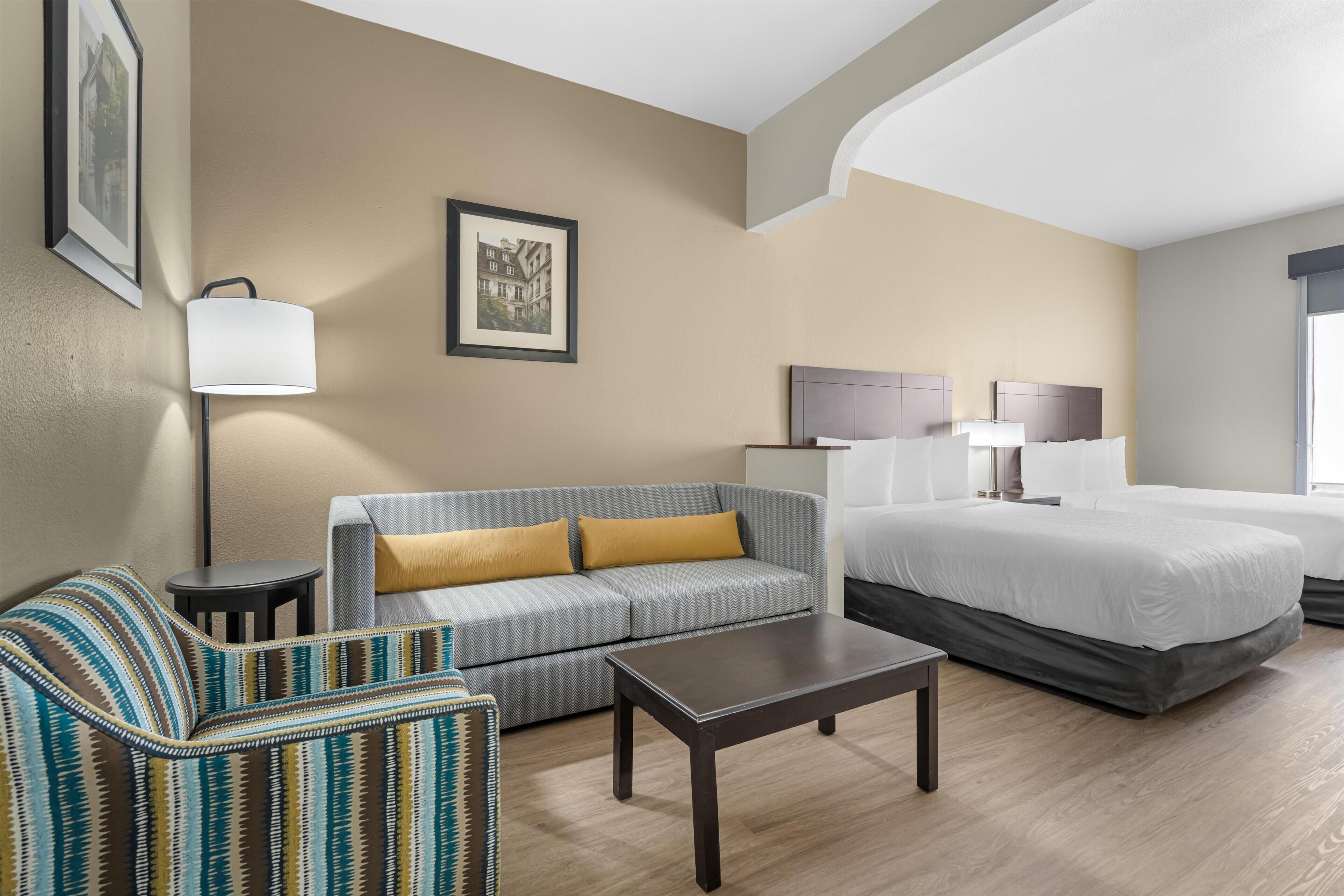 A hotel room with a bed, a sofa, a coffee table, a lamp, and framed pictures on the wall.